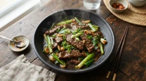 Glossy Mongolian beef with green onions in a black bowl on a dark wooden table.