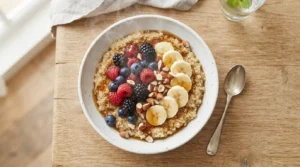 White ceramic bowl filled with warm quinoa, topped with vibrant red and blue berries, yellow banana slices, and crunchy almonds, drizzled with maple syrup.