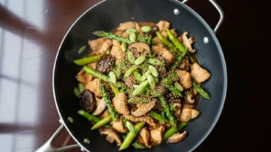 Vibrant ginger chicken stir fry with green asparagus, brown shiitake, and a glossy sauce in a black wok.